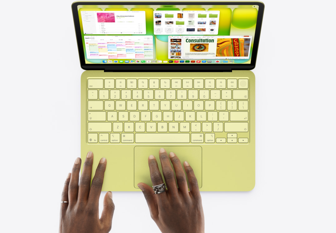 MacBook Neo, цвят цитрус, човешка ръка върху тракпада, множество отворени прозорци, включително приложенията Музика, Календар и Microsoft PowerPoint 