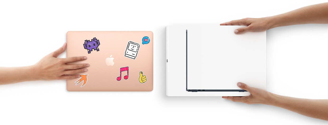 Una mano tiene un MacBook coperto di adesivi e lo fa scivolare verso la confezione di un MacBook nuovo tenuta da due mani