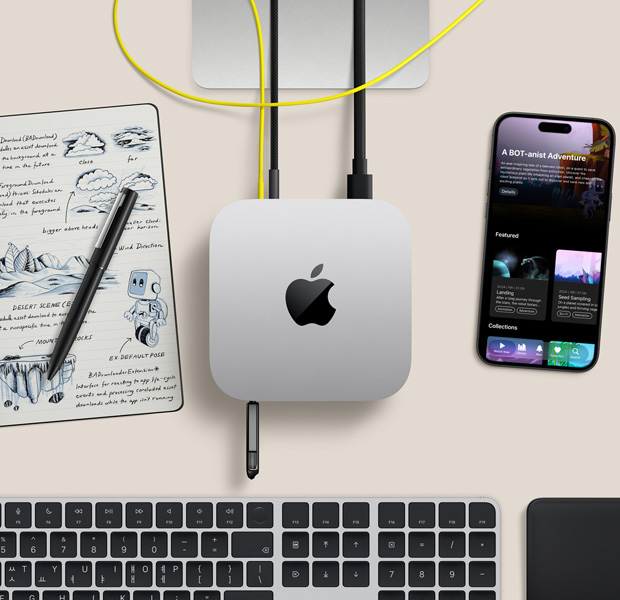 Mac mini를 위에서 바라본 모습. 실버 알루미늄 외장, 둥근 형태의 모서리, 중앙의 광택 나는 검은색 Apple 로고가 보이며, 코드가 연결되어 있고, 전면에 있는 USB-C 포트에 USB 스틱이 꽂혀 있습니다. Studio Display 스탠드의 일부가 보이며, iPhone, Magic Trackpad, Touch ID 탑재형 Magic Keyboard, 스타일러스, 전자 잉크 스케치 패드가 함께 놓여 있습니다.