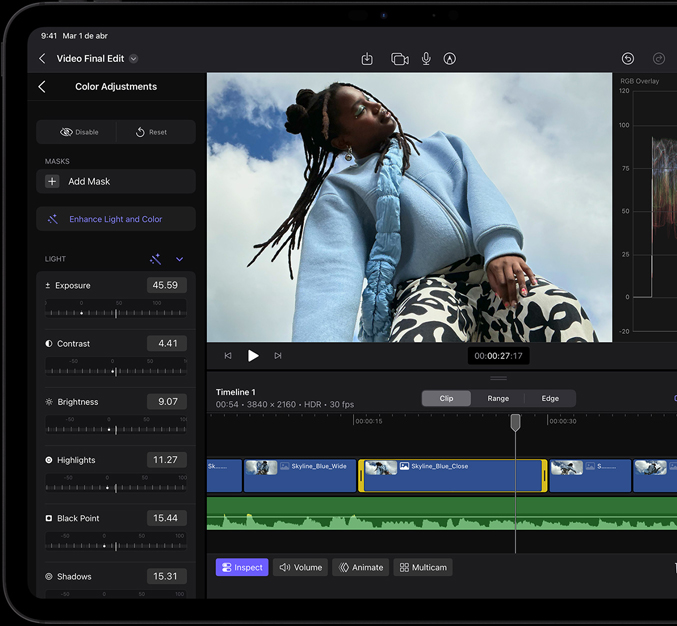 Un iPad Pro, parte frontal, marco de la pantalla negro, la pantalla muestra una app de edición de video con una foto de una persona modelando un saco azul y pantalones blanco con negro, el panel de ajuste de color está abierto a la izquierda con varios efectos de video y reguladores, línea de tiempo en la parte inferior con múltiples clips de video y pistas de audio