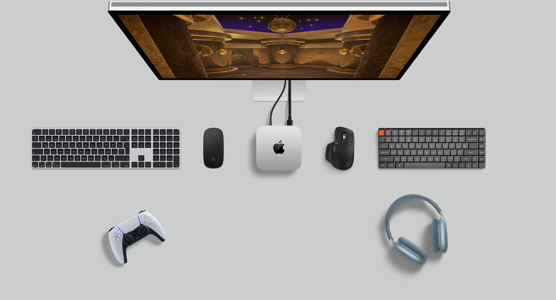 Mac mini, Studio Display, kablosuz klavyeler, kablosuz mouse’lar, bir oyun kumandası ve AirPods Max’in bulunduğu masa düzeninin üstten görünümü