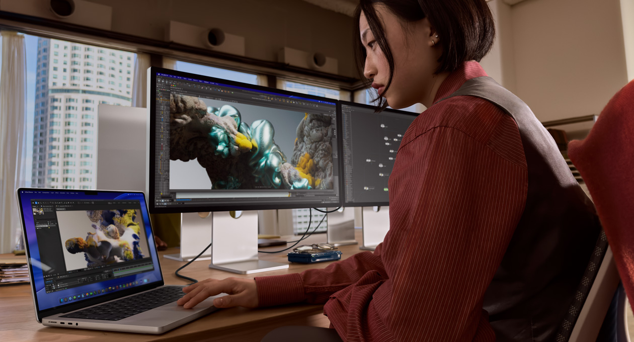 Людина в офісі працює на ноутбуку MacBook, підключеному до монітора Studio Display XDR через порт Thunderbolt 5