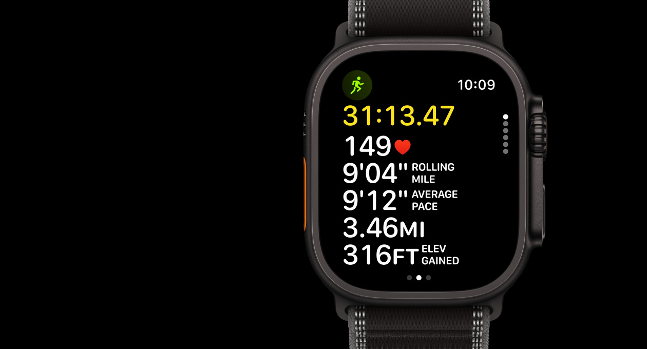 Apple Watch Ultra 3 med urkasse av svart titan og Trail Loop i svart/koksgrå. På skjermen vises Trening-appen med en aktiv treningsøkt for løping utendørs. På venstre side av urkassen vises handlingsknappen, og på høyre side vises Digital Crown og sideknappen.