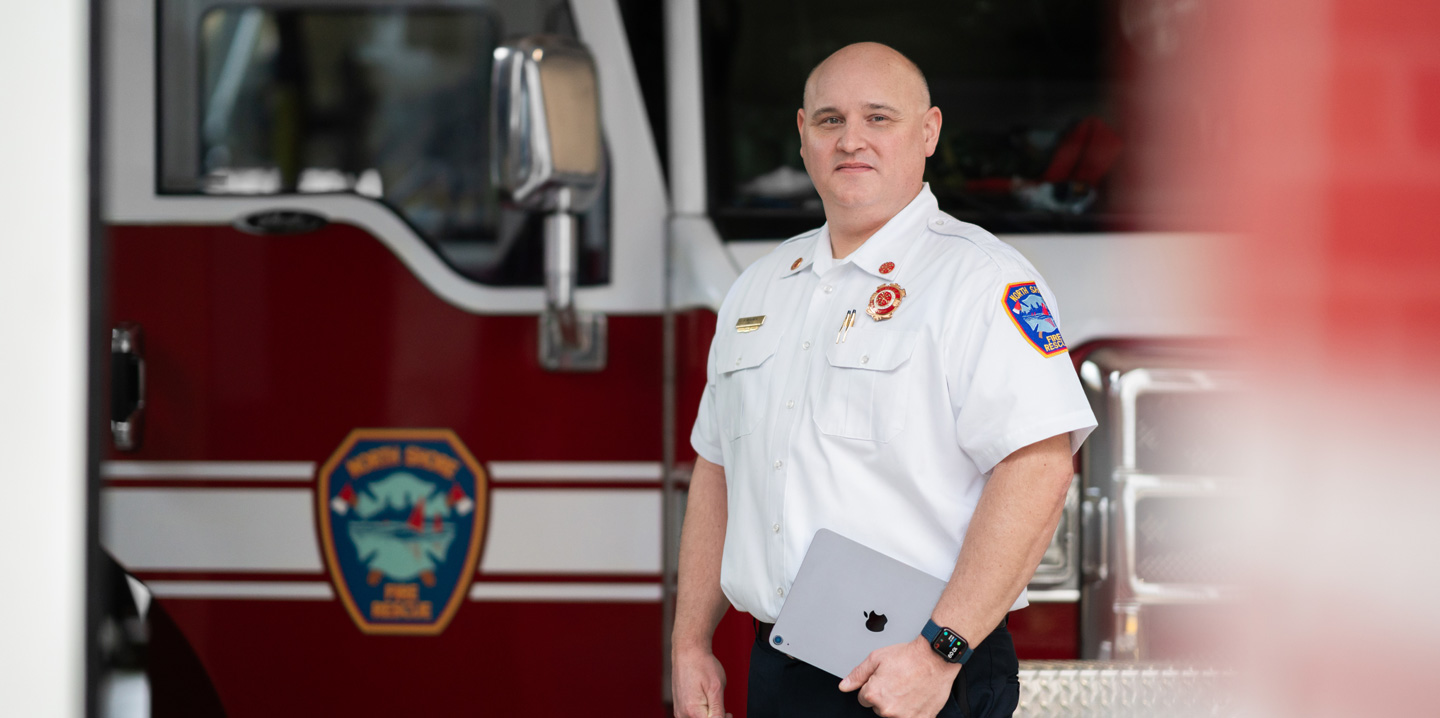 The fire chief stands in front of a fire engine holding an iPad and wearing an Apple&nbsp;Watch