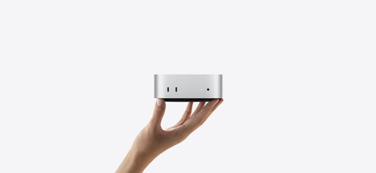 Front view of Mac mini balanced on the fingertips of an up-stretched hand, front shows two Thunderbolt ports, status indicator light and headphone jack, tapered black base at bottom, flat top, rounded sides, straight edges, silver color