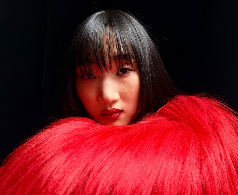一位女士身穿鮮紅羽毛上衣的近鏡特寫，展示 iPhone 17 Pro 的超高解像度拍攝功能